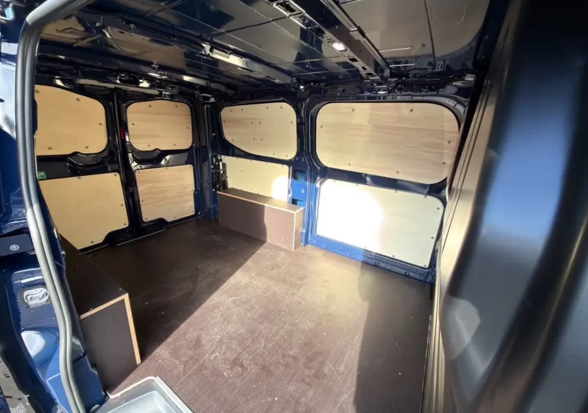 Vue intérieure arrière du Volkswagen Transporter bleu 2025 avec aménagement bois et espace de chargement vide.
