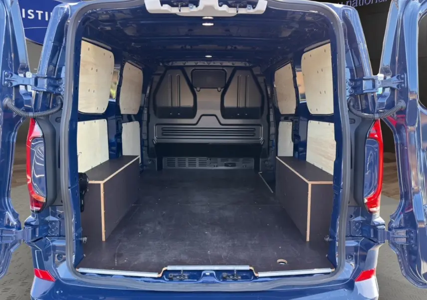 Vue arrière du Volkswagen Transporter bleu 2025 avec portes ouvertes montrant l'aménagement bois intérieur du coffre.