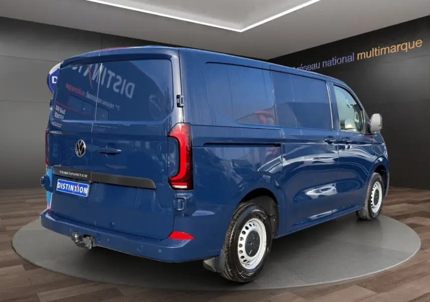 Vue 3/4 arrière droite du Volkswagen Transporter bleu avec attelage et jantes acier blanches en showroom.