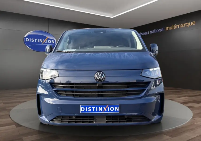 Vue frontale d'un Volkswagen Transporter bleu 2025 avec calandre noire et logo VW centré, en showroom.