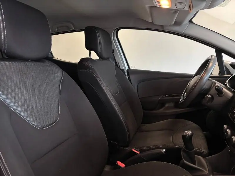 Vue intérieure côté conducteur de la Renault Clio 2014, sièges noirs avec volant cuir et levier de vitesse manuel visible.