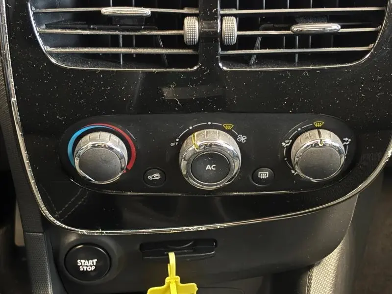Vue rapprochée des commandes de climatisation et du bouton start/stop sur la console centrale noire d'une Renault Clio gris platine 2014.