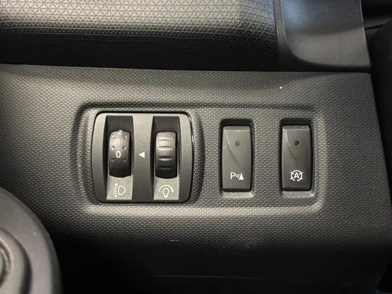 Gros plan sur les commandes de réglage des phares et aides à la conduite dans une Renault Clio gris platine 2014