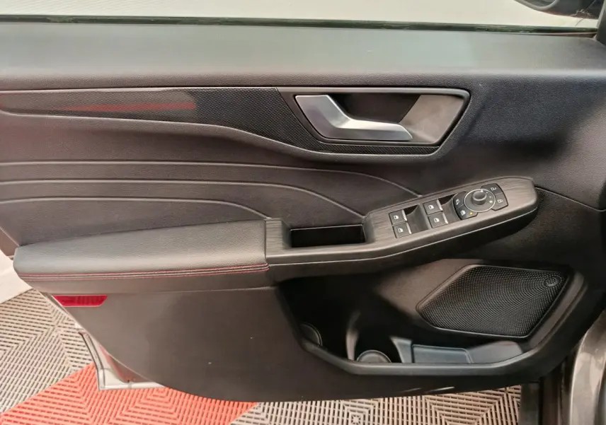 Panneau de porte avant gauche noir avec commandes électriques et surpiqûres rouges du Ford Kuga 2024 St Line.
