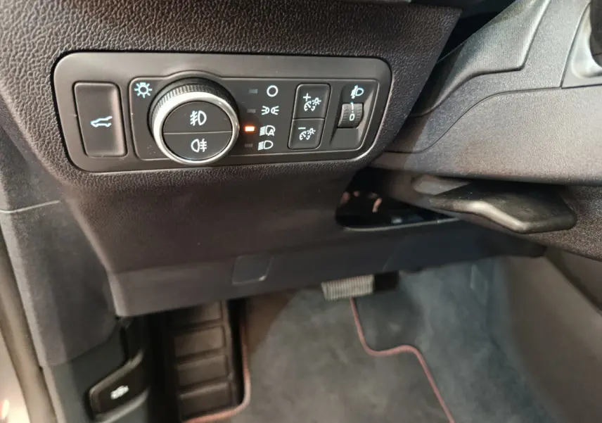 Gros plan sur les commandes d'éclairage et ouverture du coffre côté gauche du tableau de bord du Ford Kuga gris clair 2024.