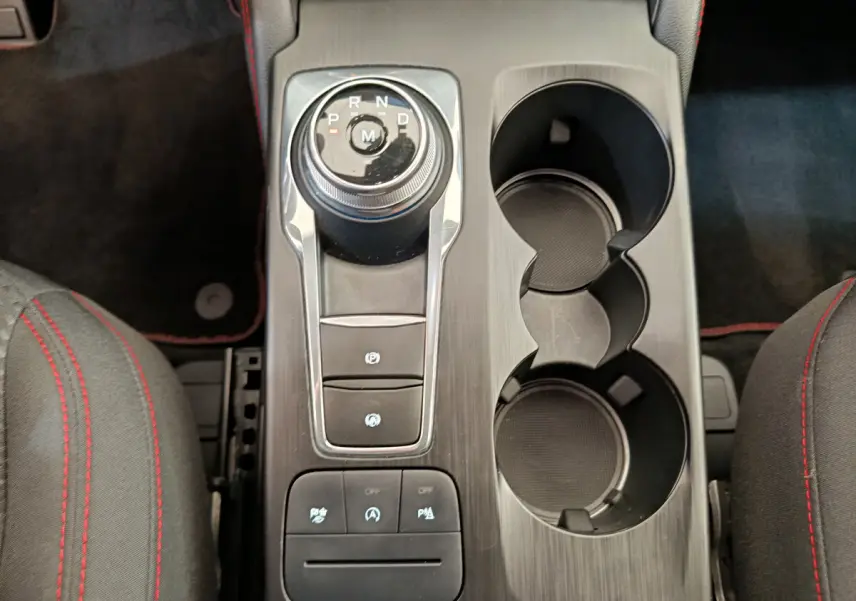 Vue plongeante sur la console centrale noire du Ford Kuga gris clair, avec molette de boîte auto et porte-gobelets.