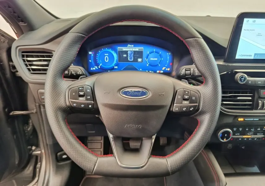 Vue rapprochée du volant cuir noir avec surpiqûres rouges et tableau de bord numérique bleu du Ford Kuga 2024 gris clair.