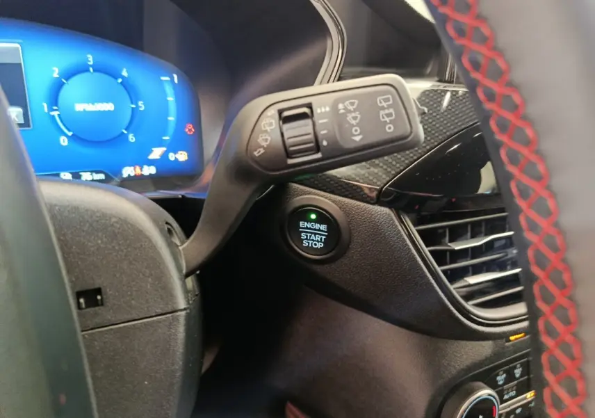 Gros plan sur le bouton start/stop et le combiné d'instruments bleu du Ford Kuga gris clair, intérieur côté conducteur.