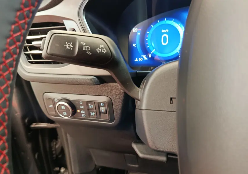 Gros plan sur le commodo gauche et le tableau de bord numérique bleu du Ford Kuga 2024 gris clair, intérieur moderne.