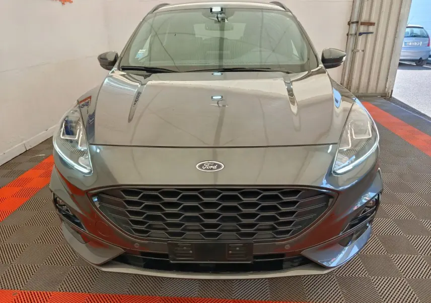 Vue frontale d'un Ford Kuga gris clair 2024 avec calandre hexagonale et phares LED allumés