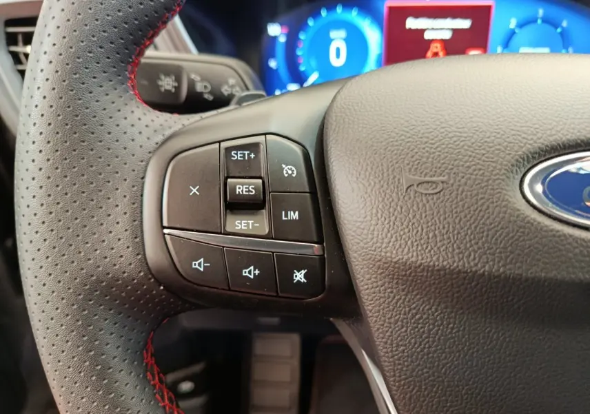 Gros plan sur le volant cuir perforé avec surpiqûres rouges du Ford Kuga 2.0 EcoBlue 2024, affichage digital en arrière-plan.