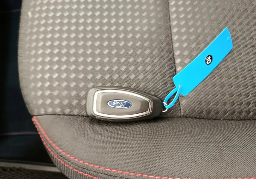 Clé Ford posée sur siège tissu gris foncé avec surpiqûres rouges, intérieur du Ford Kuga 2024 visible partiellement.