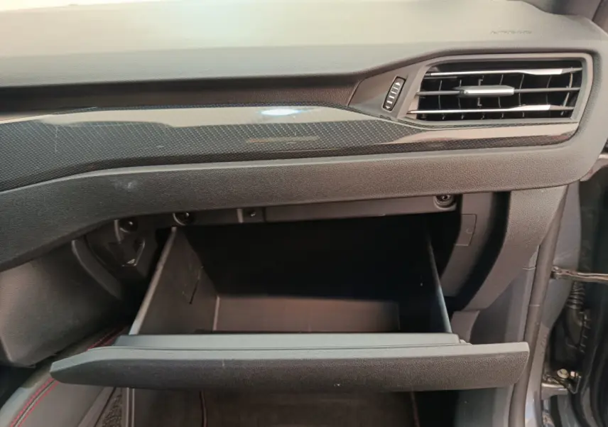 Gros plan sur la boîte à gants ouverte côté passager du Ford Kuga 2024 avec tableau de bord noir et insert carbone.