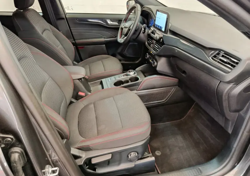 Intérieur avant droit du Ford Kuga gris clair 2024, sièges tissu avec surpiqûres rouges et écran tactile central.