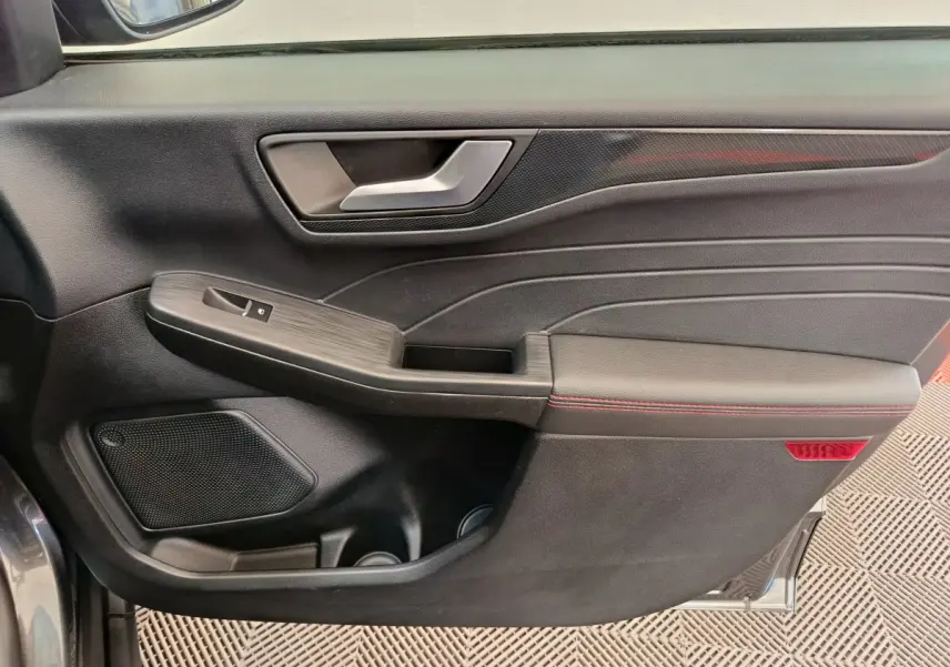 Gros plan sur la porte intérieure côté gauche du Ford Kuga gris clair, avec poignée argentée et surpiqûres rouges.