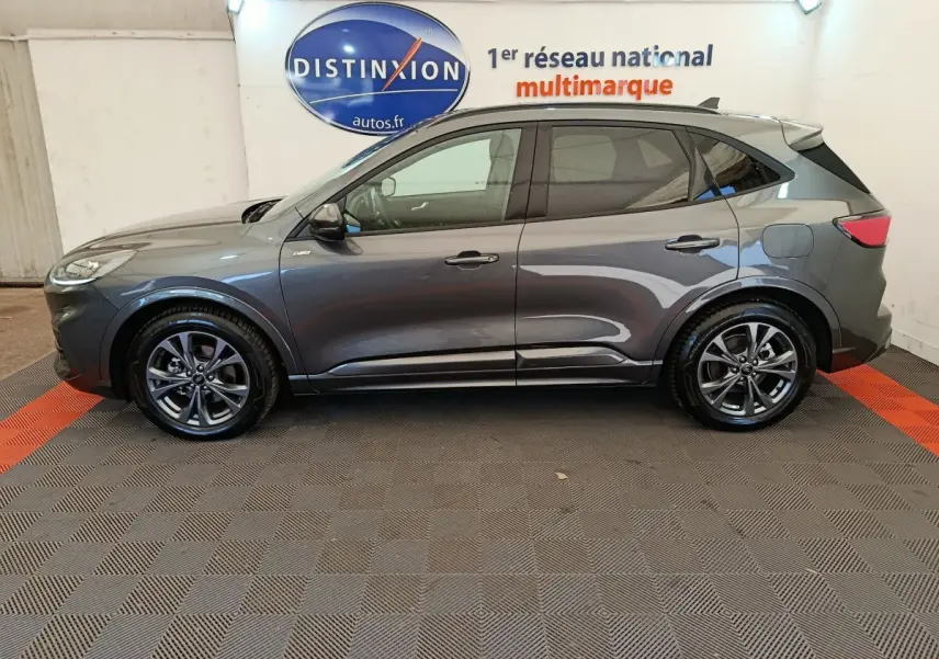 Profil côté gauche d'un Ford Kuga gris clair 2024 St Line, posé en intérieur sur sol damier avec logo Distinxion en arrière-plan.