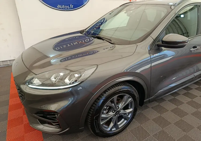 Vue 3/4 avant droit d'un Ford Kuga gris clair avec phares LED et jantes alliage au showroom.