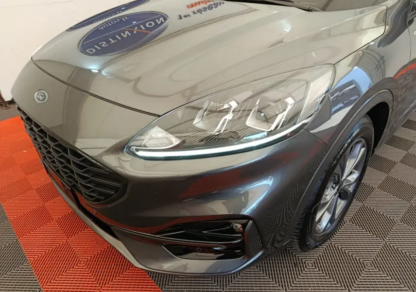 Vue 3/4 avant droit d'un Ford Kuga gris clair mettant en valeur ses phares LED et sa calandre noire.