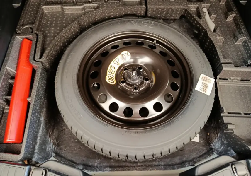 Vue plongeante sur la roue de secours noire et le rangement gris foncé du coffre du Ford Kuga gris clair 2024.