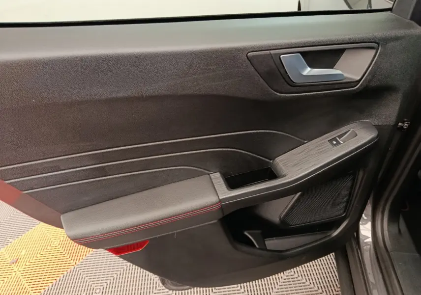 Vue côté gauche de la porte intérieure noire du Ford Kuga 2024 avec surpiqûres rouges et poignée argentée.