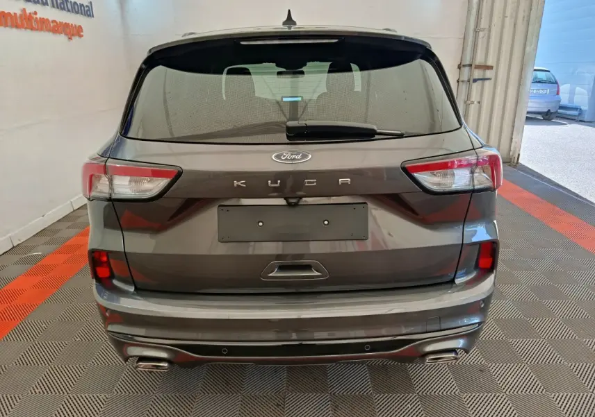 Vue arrière d'un Ford Kuga gris clair 2024 avec feux LED et double sortie d'échappement chromée dans un garage.