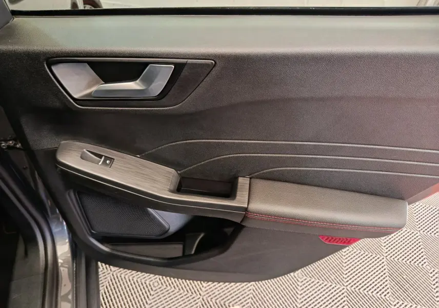 Gros plan sur la porte côté gauche du Ford Kuga gris clair, avec accoudoir noir et surpiqûres rouges visibles.