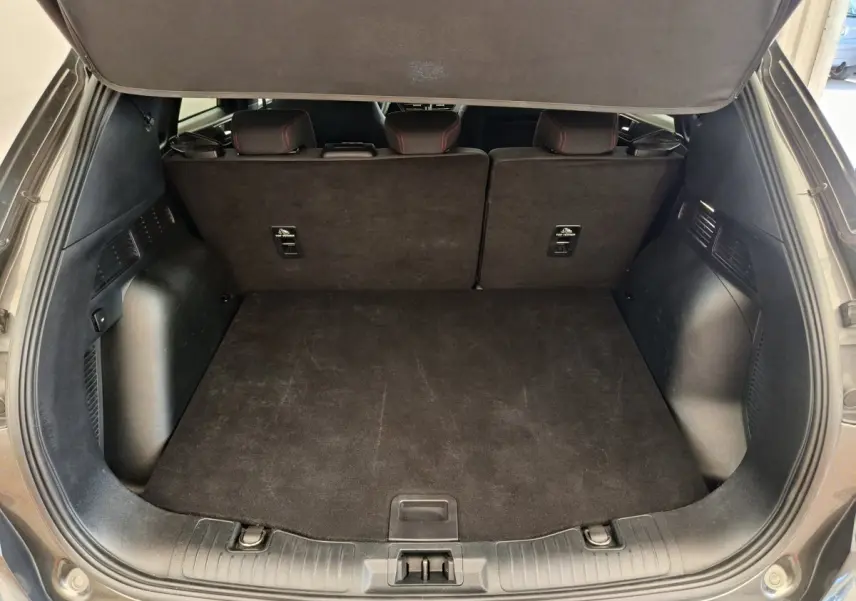 Coffre ouvert vu de l'arrière d'un Ford Kuga gris clair, banquette arrière relevée et espace de chargement vide.