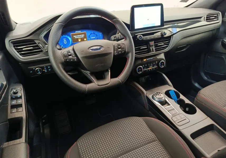 Vue intérieure avant du Ford Kuga 2024, tableau de bord noir avec écran tactile et volant cuir multifonctions.