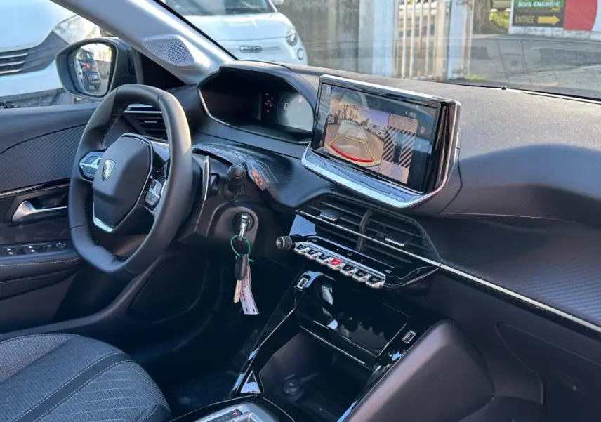 Vue intérieure côté conducteur du Peugeot 208 Hybrid blanc 2025, avec écran tactile affichant la caméra de recul et volant multifonction.