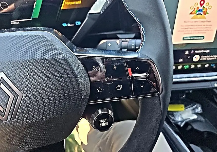 Gros plan sur le volant noir du Renault Austral blanc nacré, avec commandes multifonctions et bouton Multi-Sense visible.