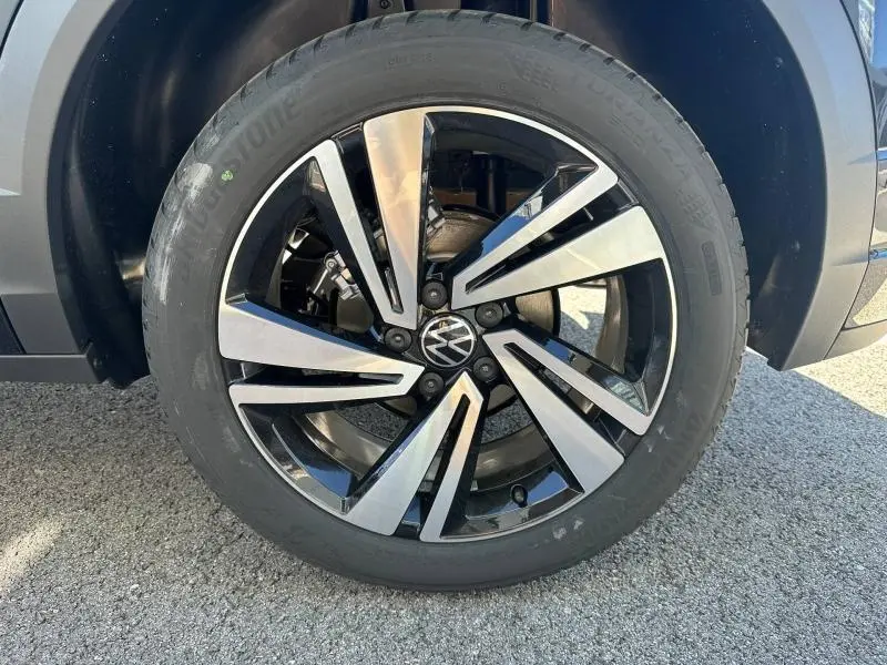 Gros plan sur la jante alu bicolore noir et argent avec logo Volkswagen, roue avant droite du T-Roc noir nacré.