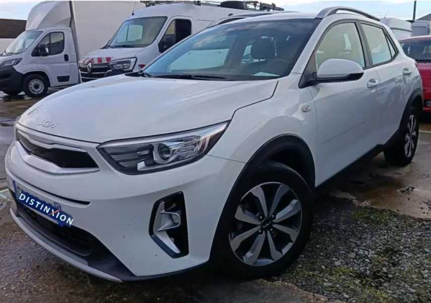 KIA Stonic blanc vue 3/4 avant droit, avec jantes alliage et calandre noire distinctive, en extérieur sur parking.