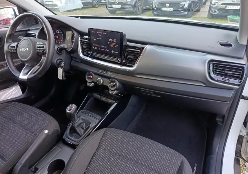 Intérieur de la KIA STONIC blanc 2022, vue côté passager montrant tableau de bord, volant et boîte manuelle.