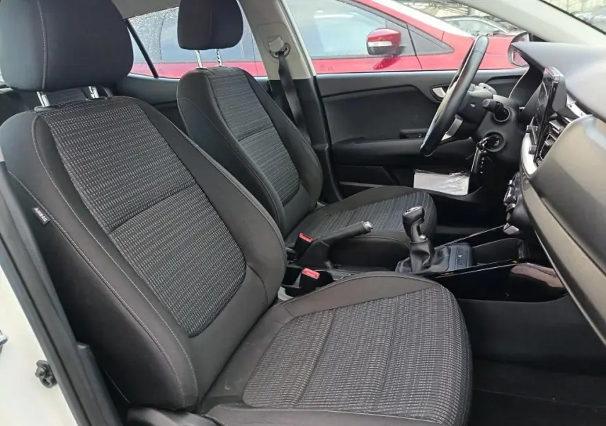 Vue intérieure côté conducteur du Kia Stonic blanc 2022, montrant les sièges tissu noirs et la boîte manuelle.