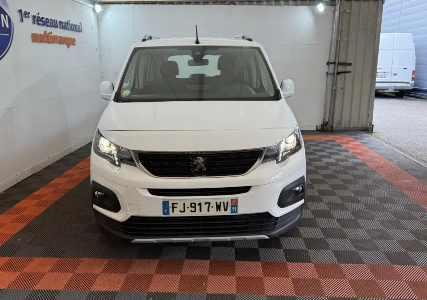Vue frontale d'un Peugeot Rifter blanc 2019 avec calandre noire et feux allumés dans un garage.