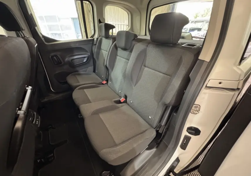 Vue intérieure côté droit sur la banquette arrière grise du Peugeot Rifter blanc, avec porte ouverte et habillage clair.