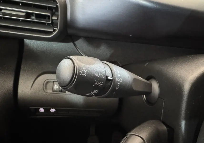 Gros plan sur la commande des feux à gauche du volant dans l’habitacle noir du Peugeot Rifter blanc 2019.