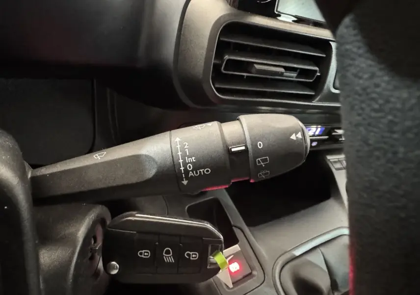 Gros plan sur la commande d’essuie-glace et la clé insérée du Peugeot Rifter blanc, tableau de bord partiellement visible.