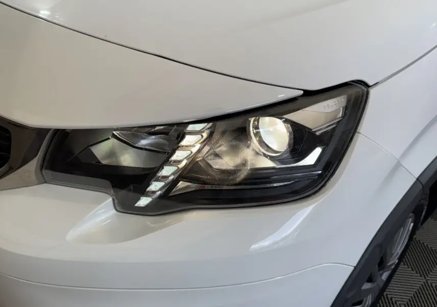 Gros plan sur le phare avant droit du Peugeot Rifter blanc, mettant en valeur les LED diurnes et la carrosserie lisse.