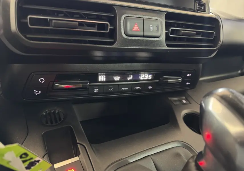 Gros plan sur la console centrale noire du Peugeot Rifter blanc, montrant la climatisation digitale et le frein à main électrique.