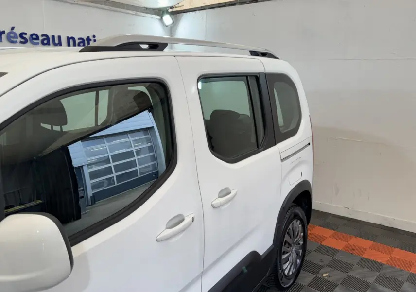Vue latérale droite d’un Peugeot Rifter BlueHDi 100 Allure blanc, avec barres de toit et jantes alliage visibles.