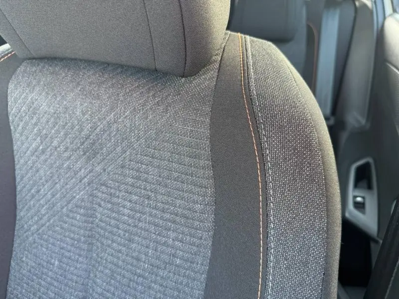 Gros plan sur le siège avant tissu gris avec surpiqûres orange de la Peugeot 308 2025 blanc Okénite.