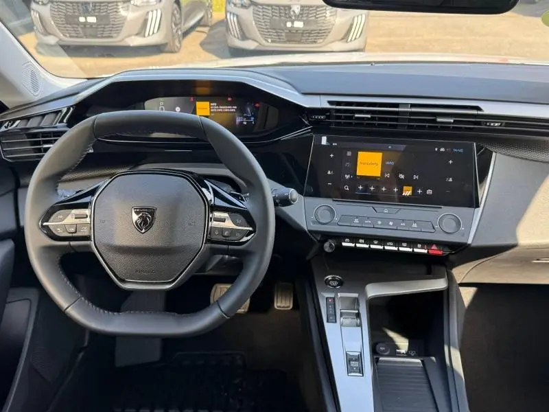 Vue intérieure du poste de conduite de la Peugeot 308 2025, volant multifonction et écran tactile central visibles.