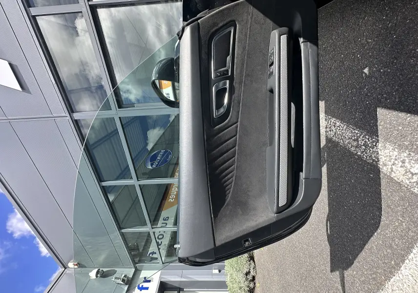 Portière côté gauche ouverte d'une Mercedes AMG GT gris foncé, montrant l'intérieur en alcantara et inserts carbone.