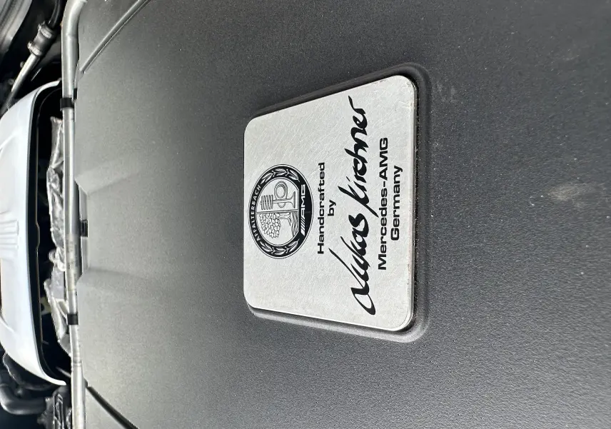 Gros plan sur la plaque du moteur gris foncé d'une Mercedes AMG GT 4.0 V8 510 S, soulignant l'artisanat allemand.