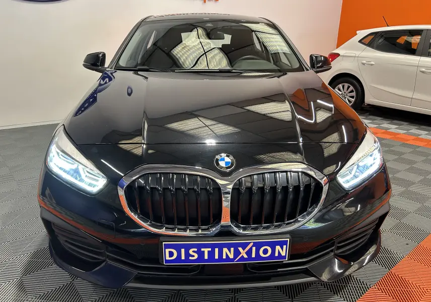 Vue avant d'une BMW Série 1 noire 2023 avec phares LED allumés et calandre caractéristique en double haricot.