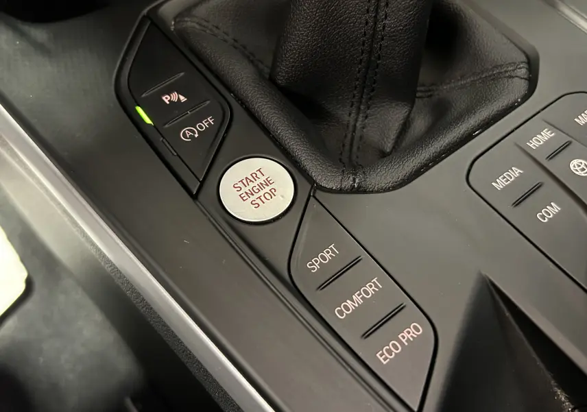 Gros plan sur la console centrale noire de la BMW Série 1 16d 2023, montrant les boutons de mode de conduite et le bouton Start Engine Stop.