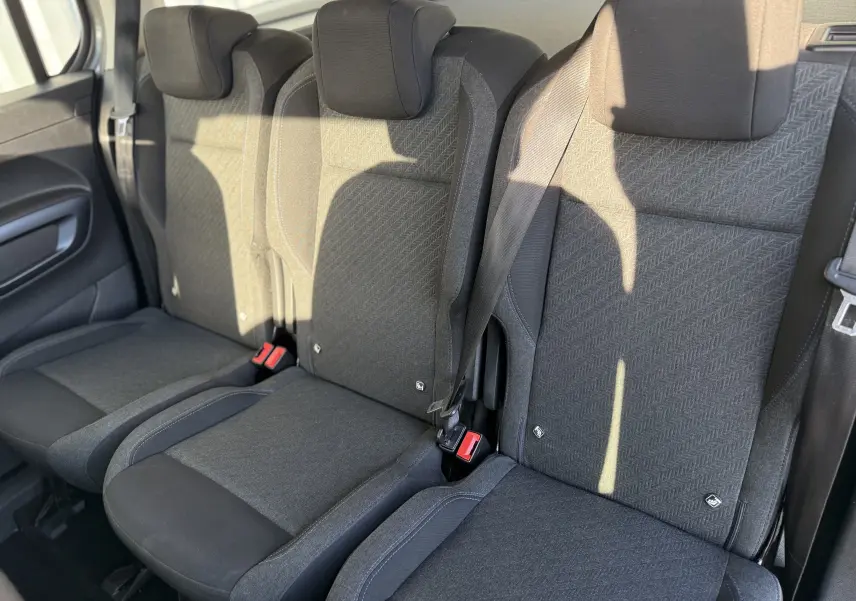 Vue intérieure des sièges arrière en tissu gris foncé du Peugeot Rifter 1.5 BlueHDi 130 Allure 7 places, avec ceintures visibles.