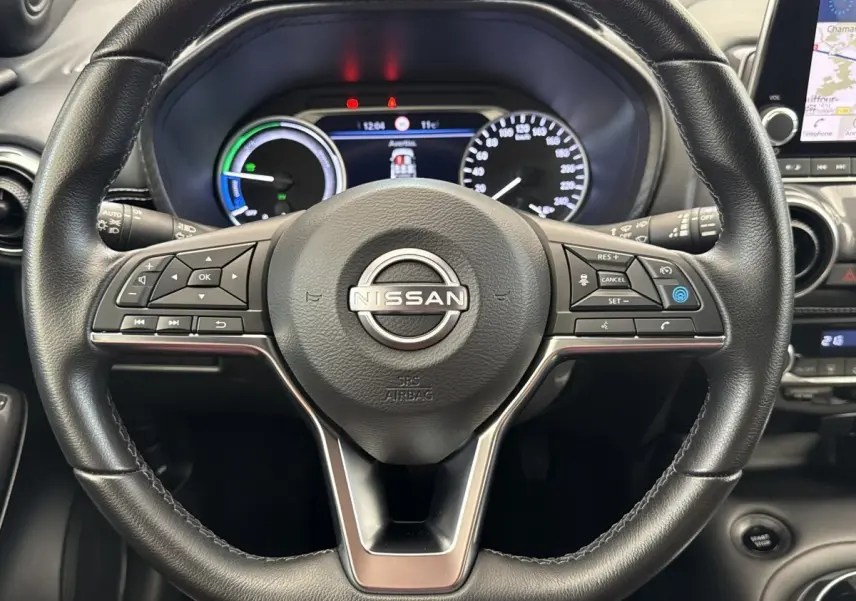 Vue rapprochée du volant noir d’un Nissan Juke 2023 avec tableau de bord numérique et écran tactile de navigation visible à droite.