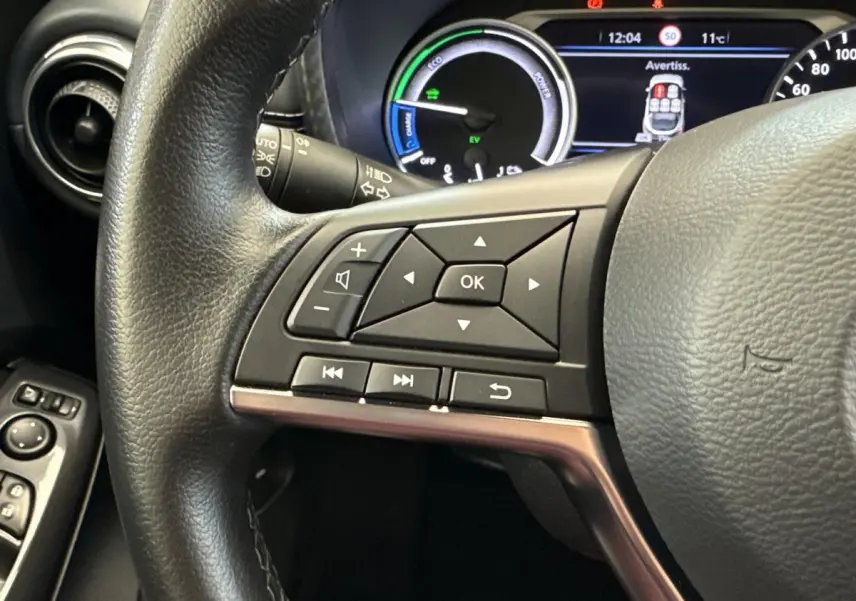 Gros plan sur le volant noir du Nissan Juke 2023 avec commandes multifonctions et tableau de bord numérique en arrière-plan.
